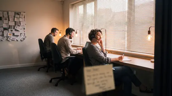 A charity supporter care team on headsets at a shared desk in the early evening.