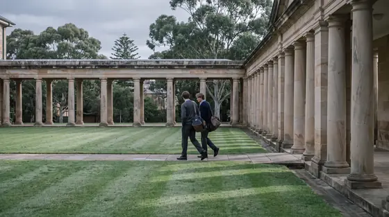 Two students walking through a sandstone school colonnade in early morning light.